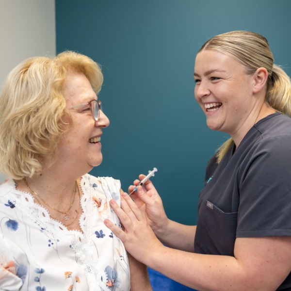 A Praxis Medical team member smiling and giving an injection to a patient